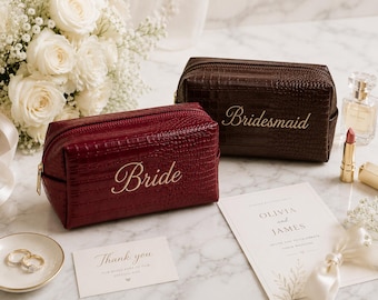 May include: A deep red cosmetic bag with a crocodile texture and the word Bride in gold script, and a dark brown cosmetic bag with a crocodile texture and the word Bridesmaid in gold script, both featuring gold zippers and rectangular shapes.