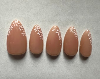 May include: Set of six nude-coloured false nails with white floral designs.