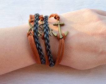 May include: A layered bracelet with brown leather and black braided cord. The bracelet features a metal anchor and a metal steering wheel charm.