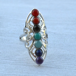 May include: A silver ring with a delicate design featuring seven colorful gemstones in a vertical row. The stones are red, orange, yellow, green, blue, indigo, and violet, representing the seven chakras.