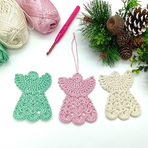 May include: Three crocheted angel ornaments in green, pink, and white. The ornaments are hanging from white string and are on a white background.