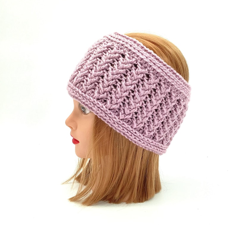 May include: A lavender knitted headband with a textured pattern. The wide band is designed to cover the forehead and ears. The headband is shown on a mannequin head with blonde hair and a white background.