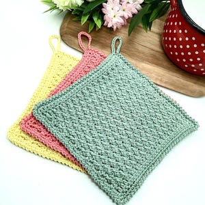 May include: Three crocheted pot holders in yellow, pink, and green. The pot holders are square shaped and have a loop handle.