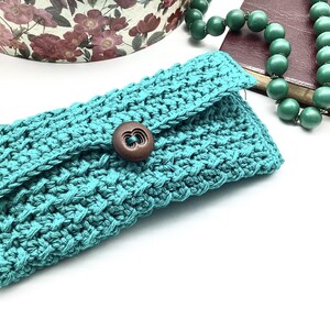 May include: A teal crocheted clutch with a brown button closure.