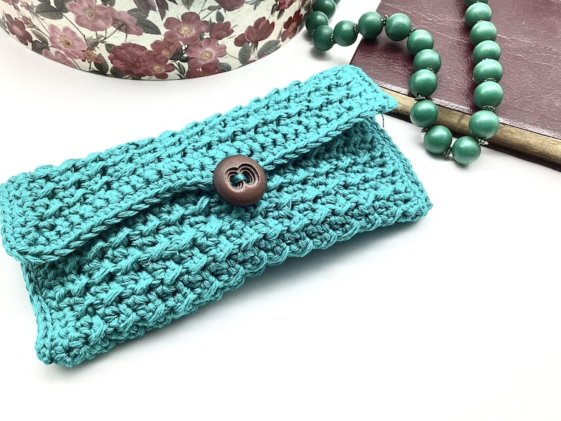 May include: A teal crocheted clutch with a brown button closure.