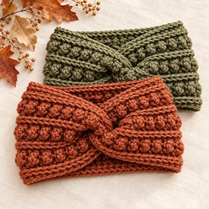 May include: Two crochet headbands featuring a twisted front design and a textured bobble stitch pattern. One headband is olive green and the other is a burnt orange colour. Both items are crafted with thick yarn and have a wide, ribbed construction.