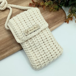 May include: A crocheted cream-coloured phone pouch with a brown leather tag that says "Hand Made" with a butterfly design.