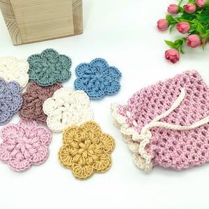 May include: A set of eight crocheted flower-shaped coasters in various colors, including pink, blue, green, yellow, and white. The coasters are arranged in a circle on a white surface.