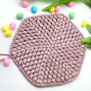 Könnte beinhalten: Ein rosa gehäkelter sechseckiger Untersetzer mit einer strukturierten Oberfläche. Der Untersetzer ist mit einer festen Masche gehäkelt und hat eine leicht erhöhte Mitte.
