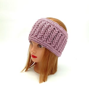 May include: A mauve knitted headband with a textured design. The headband is shown on a mannequin head with red lips and auburn hair. The wide band is likely for warmth or fashion, and is a soft, muted colour.