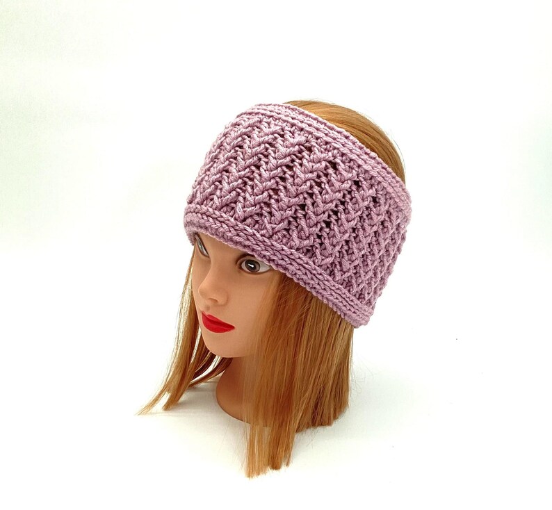 May include: A mauve knitted headband with a textured design. The headband is shown on a mannequin head with red lips and auburn hair. The wide band is likely for warmth or fashion, and is a soft, muted colour.