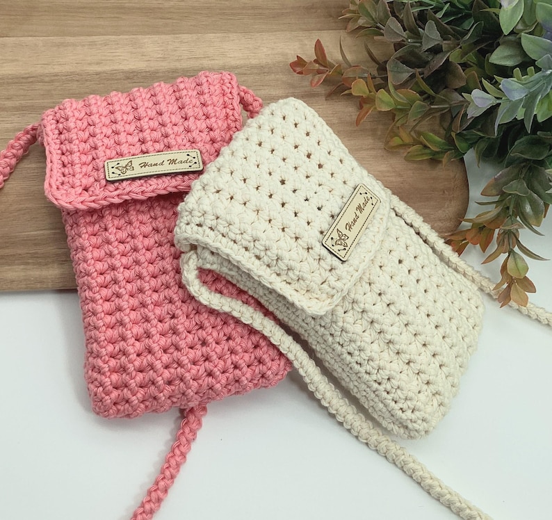 May include: Two crocheted phone pouches, one pink and one cream, with a wooden tag that says "Hand Made".