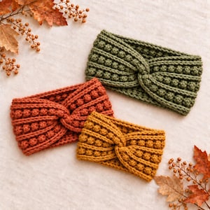 May include: Three crocheted headbands in olive green, burnt orange, and mustard yellow. Each headband features a central twist detail and a textured bobble stitch pattern throughout the knit, creating a thick and uniform appearance.