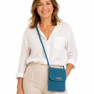 Pu&ograve; includere: Borsa a tracolla all'uncinetto blu turchese con chiusura a patta e tracolla lunga. La borsa ha una piccola etichetta metallica rettangolare sul davanti. La borsa &egrave; indossata a spalla.