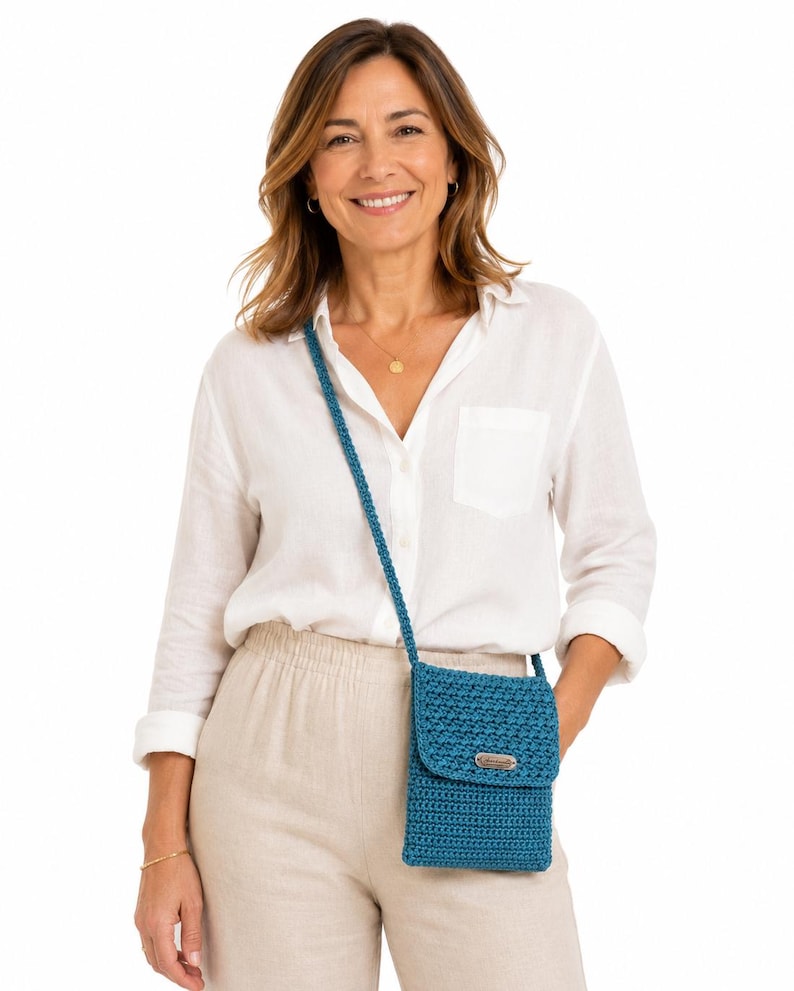 Pu&ograve; includere: Borsa a tracolla all'uncinetto blu turchese con chiusura a patta e tracolla lunga. La borsa ha una piccola etichetta metallica rettangolare sul davanti. La borsa &egrave; indossata a spalla.