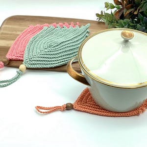 May include: Three crocheted pot holders in the shape of leaves. One is green, one is pink, and one is peach. The pot holders have wooden beads attached to the ends of the strings.