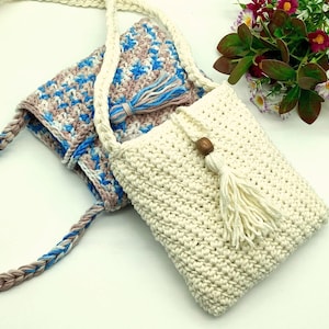 Könnte beinhalten: Zwei gehäkelte Taschen mit Quasten. Eine Tasche ist weiß mit einer braunen Perle und die andere ist blau, rosa und weiß.