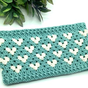 May include: A teal crocheted clutch with a white heart pattern.