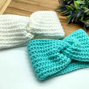 Op de afbeelding: Twee gebreide hoofdbanden, een witte en een turquoise. De hoofdbanden zijn gemaakt met een eenvoudige steek en hebben een geknoopt ontwerp.