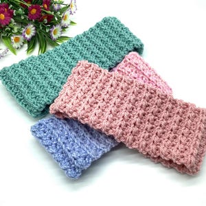 May include: Three crocheted headbands in different colors: light green, pink, and lavender. The headbands are made with a textured stitch and are folded in half.