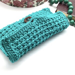 May include: A teal crocheted clutch with a wooden button closure.