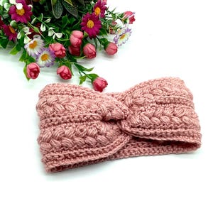 May include: A pink crocheted headband with a twisted knot design. The headband is made with a chunky yarn and has a soft, textured look.