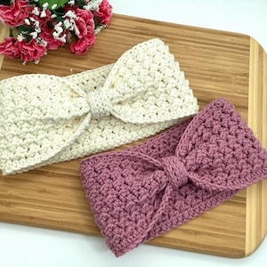 Könnte beinhalten: Zwei gehäkelte Stirnbänder mit Schleifen-Details. Ein Stirnband ist weiß und das andere ist staubig rosa.