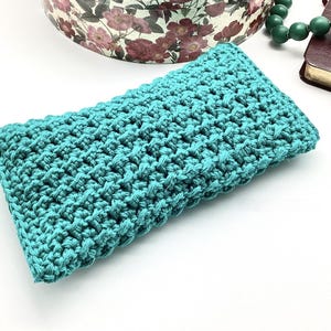 May include: A teal blue crocheted pouch or small bag. The pouch is made with a textured stitch pattern.