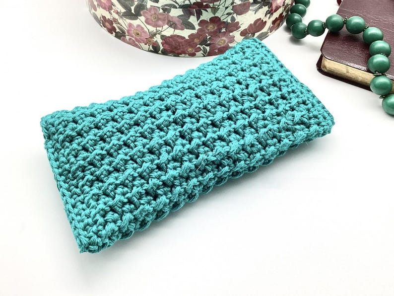 May include: A teal blue crocheted pouch or small bag. The pouch is made with a textured stitch pattern.