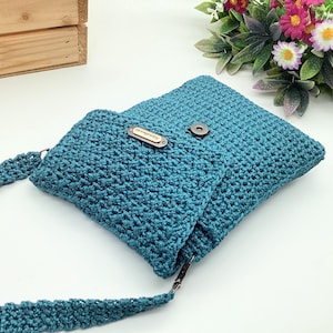 Pu&ograve; includere: Borsa a tracolla all'uncinetto color teal con chiusura a patta e tracolla lunga. La borsa presenta una piccola etichetta rettangolare con testo. &Egrave; realizzata in un materiale strutturato e intrecciato e ha una chiusura magnetica.