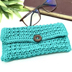 May include: Teal crocheted glasses case with a wooden button closure.