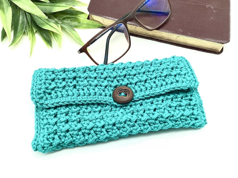 May include: Teal crocheted glasses case with a wooden button closure.