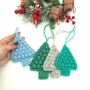 May include: Crocheted Christmas tree ornaments in shades of blue, green, and gray. Each tree has a textured, bobbled surface and a loop for hanging. Festive holiday decor.