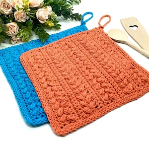 May include: Two crocheted pot holders, one in a bright turquoise blue and the other in a burnt orange colour. Both pot holders have a braided design and are made with a thick yarn.
