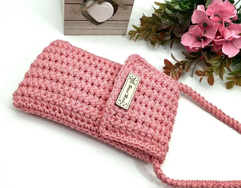 May include: A pink crocheted crossbody bag with a small brown leather tag that says "Love the Maker".