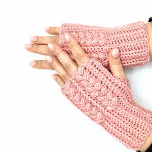 以下が含まれることがあります： ケーブル編みの模様が入ったピンクのクロシェのフィンガーレスグローブのペアです。