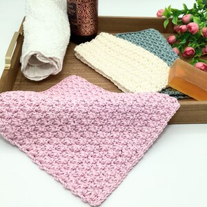 May include: Three crocheted dishcloths in pink, cream, and gray on a wooden tray with a bar of soap.