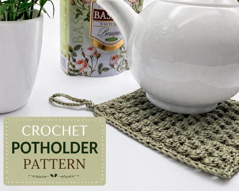 May include: A crocheted potholder in olive green with a loop handle, supporting a white teapot. The potholder has a textured, woven appearance. A label reads "CROCHET POTHOLDER PATTERN". A tea tin and a potted plant are in the background.