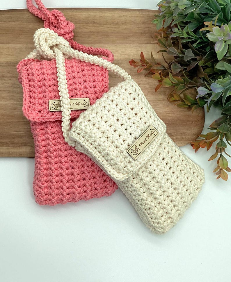 May include: Two crocheted phone pouches with straps, one in pink and one in cream, both with a brown leather tag that says "Hand Made".