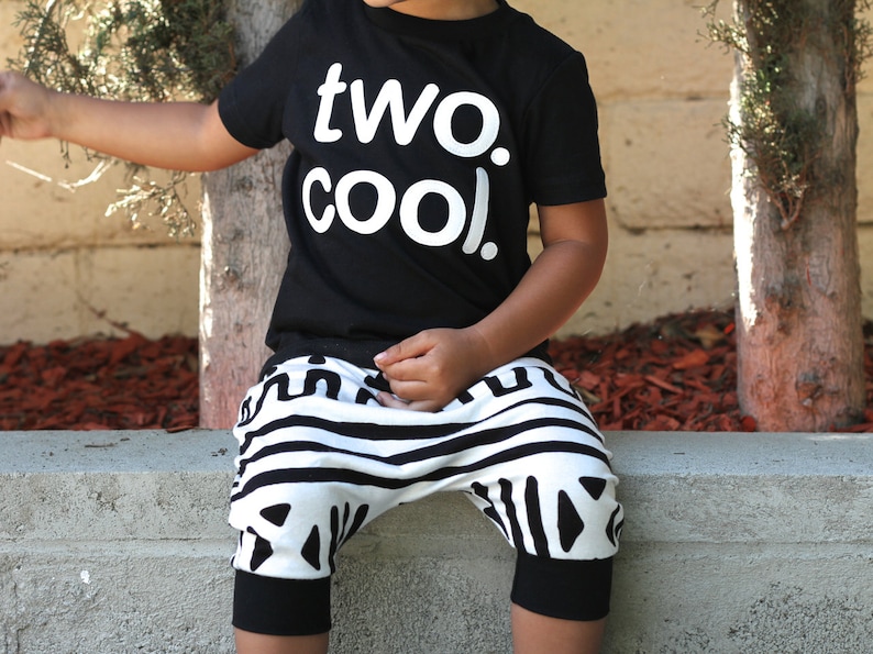 Puede incluir: Un ni&ntilde;o con una camiseta negra con el texto "two. cool." en letras blancas y pantalones a rayas blancas y negras.