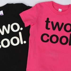 Puede incluir: Dos camisetas, una negra y otra rosa, con el texto "two. cool." impreso en ellas. La camiseta negra tiene texto blanco y la camiseta rosa tiene texto negro.