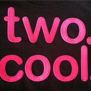 Puede incluir: Una camiseta negra con las palabras "two. cool." en letras de fieltro rosa.