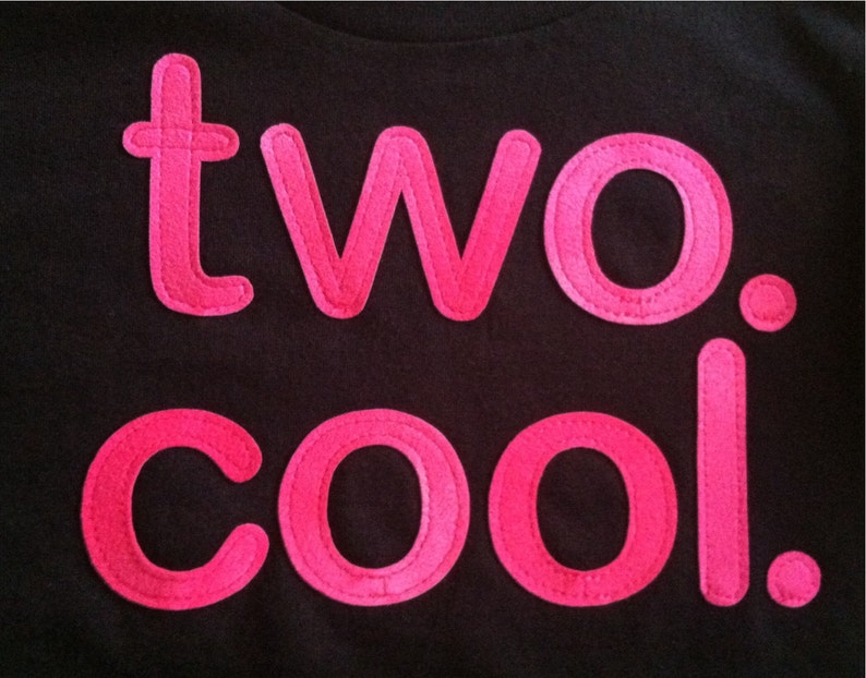 Puede incluir: Una camiseta negra con las palabras "two. cool." en letras de fieltro rosa.