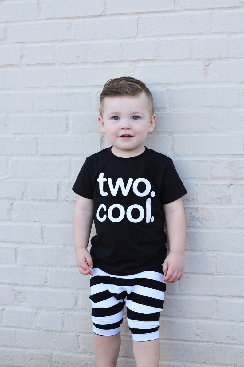 Puede incluir: Un ni&ntilde;o peque&ntilde;o con una camiseta negra con el texto "two. cool." en letras blancas. Tambi&eacute;n lleva pantalones cortos a rayas blancas y negras.
