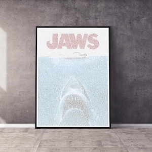 May include: A poster featuring the word "JAWS" in large pink letters at the top. The rest of the poster is made up of smaller pink letters that form the image of a shark's mouth with a person swimming above it.