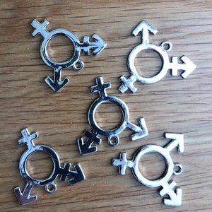 May include: Five silver-toned metal charms in the shape of the transgender symbol. Each charm features a circle with a cross and an arrow.