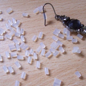 May include: A large quantity of small, clear, plastic earring backs scattered on a light wood surface.