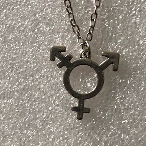 Op de afbeelding: Een zilveren ketting met een transgender symbool hanger.