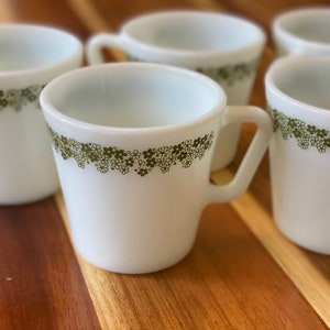 May include: Set of six white ceramic mugs with a green floral pattern around the rim.