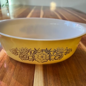 May include: A yellow ceramic baking dish with a white interior and a brown floral design around the rim.